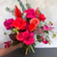 The Florist Choice - Red Nina Bouquet by FlowersonNortonSt showcases Red Nina roses with seasonal blooms in bright pink, red, orange, and purple hues, accented with eucalyptus leaves, all beautifully arranged against a light gray background.