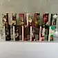 A display of 12 rectangular boxes featuring the KEW Hand Cream collection by Flowers on Norton St, adorned with intricate floral and botanical illustrations. They are arranged in rows on a white surface with a textured gray wall in the background.