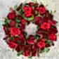 The Remembrance Wreath by FlowersonNortonSt beautifully displays vivid red roses, deep burgundy blooms, and lush green foliage on a light gray background, creating an ideal tribute.
