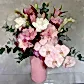 The Blush Pink Mixed Vase from Flowers on Norton St features a beautiful arrangement of pink and white seasonal flowers like orchids, lilies, and roses in a ribbed vase, accented with green eucalyptus leaves, set against a neutral textured background.