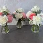Three Lovely Vintage Vases by FlowersonNortonSt are elegantly displayed on a gray surface, each filled with a table centerpiece of white and pink roses, chrysanthemums, and seasonal blooms. The greenery provides a charming contrast against the light textured background.