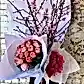 The "Colour Me Pink Seasonal Flowers" arrangement by Flowers on Norton St features peach blossoms at the center, flanked by a bouquet of seasonal pink and white roses on one side and bright pink hydrangeas on the other, all elegantly wrapped in white paper set against a textured brick wall.