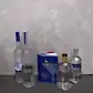 An artfully arranged Vodka Gift Set from Flowers on Norton St is displayed on a surface, showcasing bottles of Grey Goose, Belvedere, Anjea, and Absolut. Amidst the bottles stands a blue booklet titled "Vodka Made Me Do It" against a textured wall.