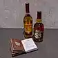 Two bottles of Scotch Whisky from Flowers on Norton St adorn the table. An open book filled with cocktail recipes and tips lies before them, set against a textured, light-colored wall.