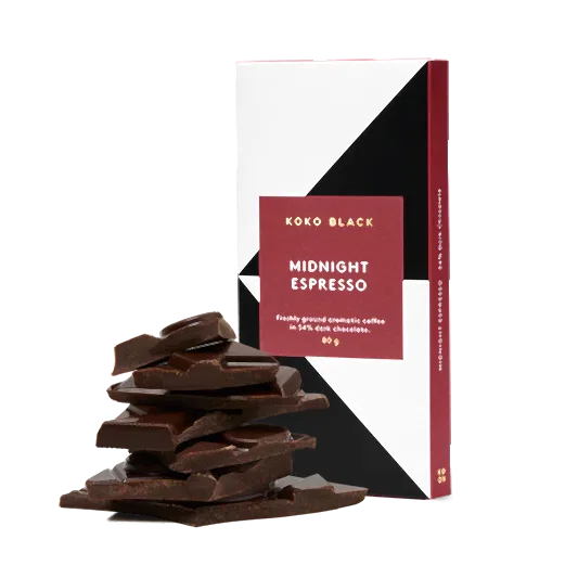 A stylishly designed chocolate bar labeled "Koko Black Midnight Espresso Chocolate" from Flowers on Norton St is pictured beside a stack of pure espresso dark chocolate pieces. This indulgent treat is infused with freshly ground aromatic coffee and features geometric patterns on its packaging.