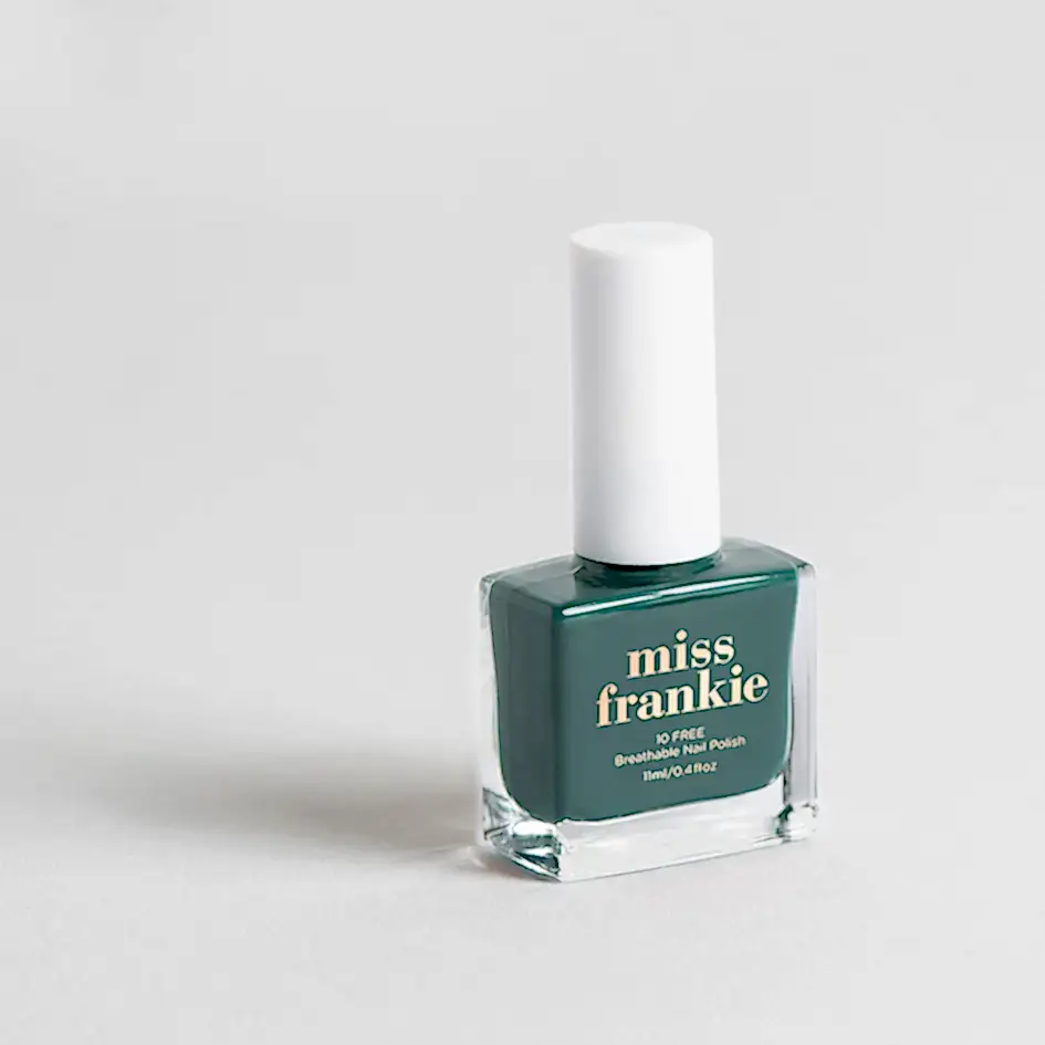 A bottle of "MISS FRANKIE" nail polish from Flowers on Norton St, featuring a green hue and a white cap, is set against a light gray backdrop. The text on the bottle reads "10 Free Breathable Nail Polish.