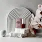 A bottle of MISS FRANKIE Nail Polish by Flowers on Norton St, along with its box, is artfully displayed on textured white stones. The composition features a white arched backdrop and pink orchids that add elegance to the scene. The light pink, chip-resistant nail polish harmoniously matches the hue of the orchids and the packaging.
