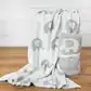 On a wooden surface, two cozy Ellie Baby Blankets from FlowersonNortonSt with adorable gray and white elephant patterns are displayed. One blanket is draped over a ledge, while the other is rolled up and tied with a white ribbon, highlighting their soft texture.