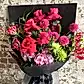 The Summer Splice Pink Bouquet by FlowersonNortonSt showcases a stunning collection of vibrant pink roses, Colombian roses, dahlias, and pink hydrangeas. Enhanced with green chrysanthemums and exotic flame lilies, this bouquet is elegantly presented in dark wrapping paper and makes a striking statement against a rustic brick wall background.