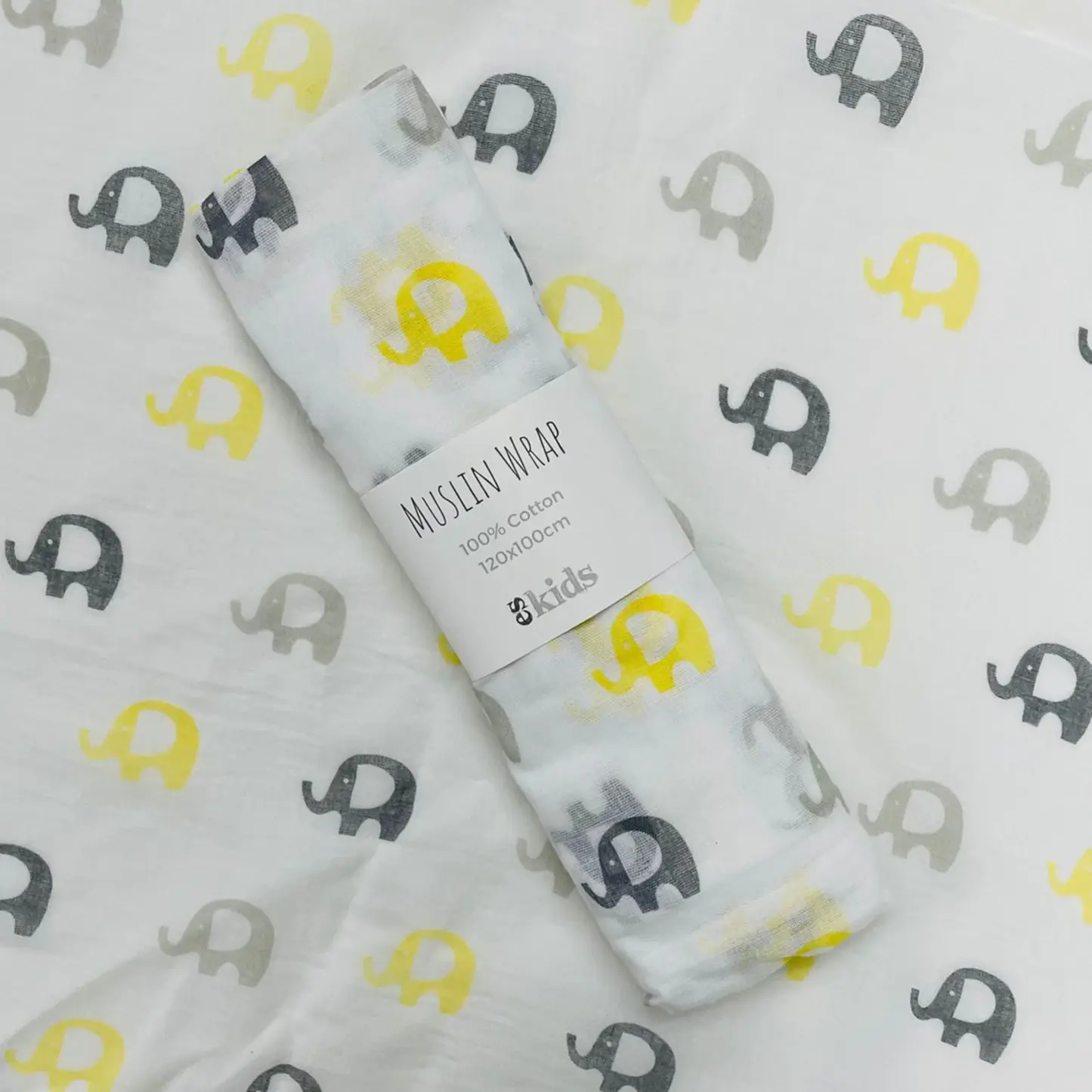 A FlowersonNortonSt Muslin Wrap features a delightful pattern of yellow, gray, and black elephants. The packaging label states, "Muslin Wraps, 100% Cotton, 120x120cm." Ideal for baby swaddling, it is set against matching elephant-patterned fabric.