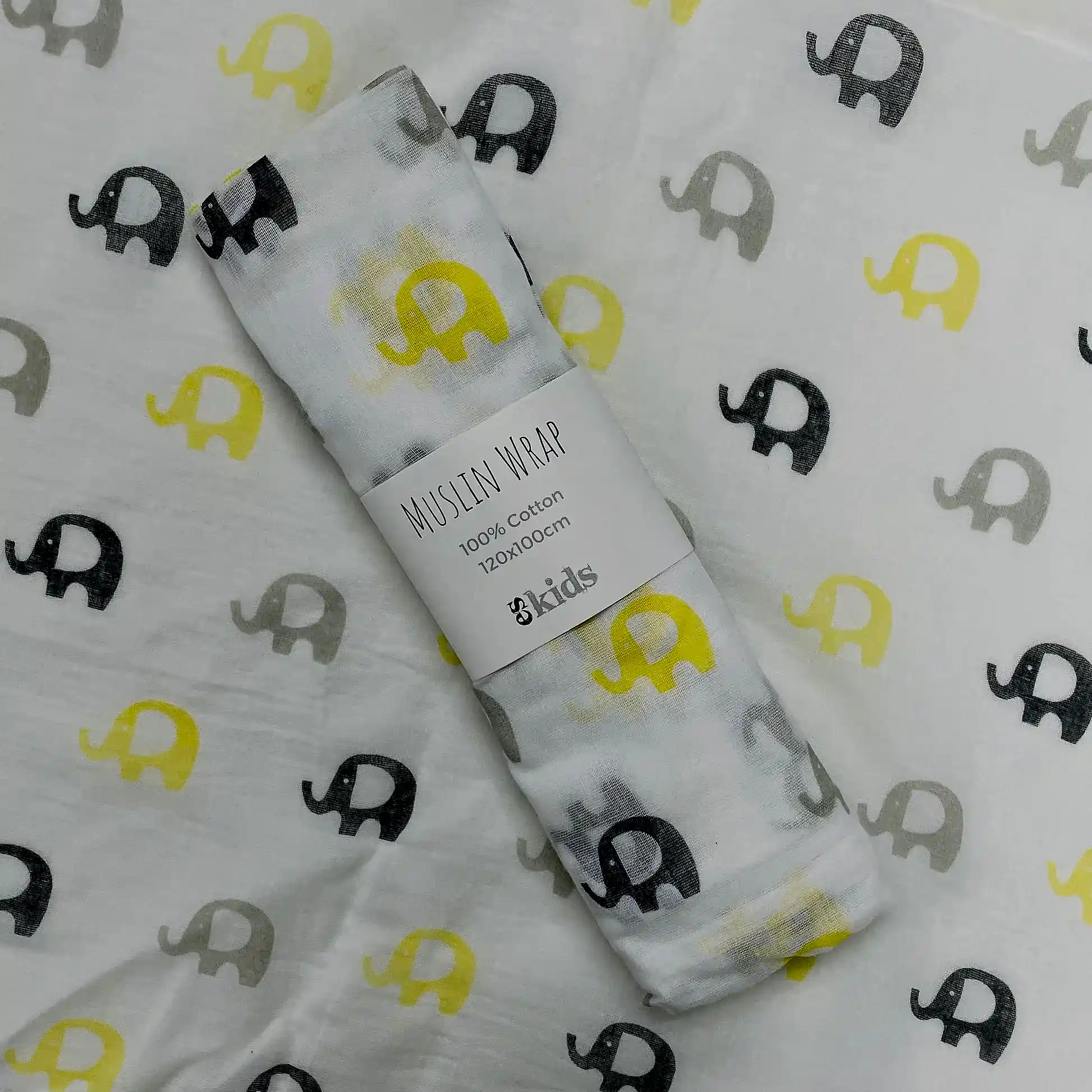 A FlowersonNortonSt Muslin Wrap features a delightful pattern of yellow, gray, and black elephants. The packaging label states, "Muslin Wraps, 100% Cotton, 120x120cm." Ideal for baby swaddling, it is set against matching elephant-patterned fabric.