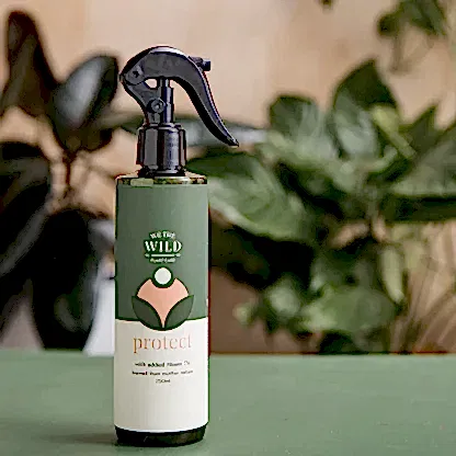 A spray bottle labeled "We The Wild - Plant Care" from the FlowersonNortonSt brand, featuring organic Neem Oil for plant care, rests on a green surface. It provides a natural solution to pest issues, with leaves appearing softly blurred in the background.