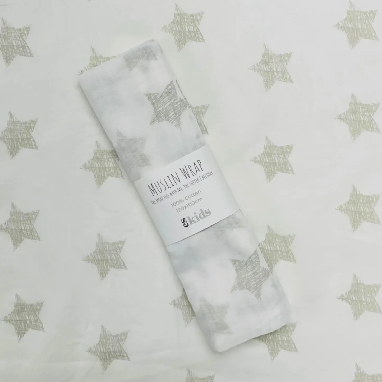 A delicately folded muslin wrap, featuring a charming star pattern, rests elegantly on coordinating fabric with the same celestial motif. The label displays "Muslin Wraps" from FlowersonNortonSt, emphasizing its 100% cotton composition—ideal for gently wrapping babies.