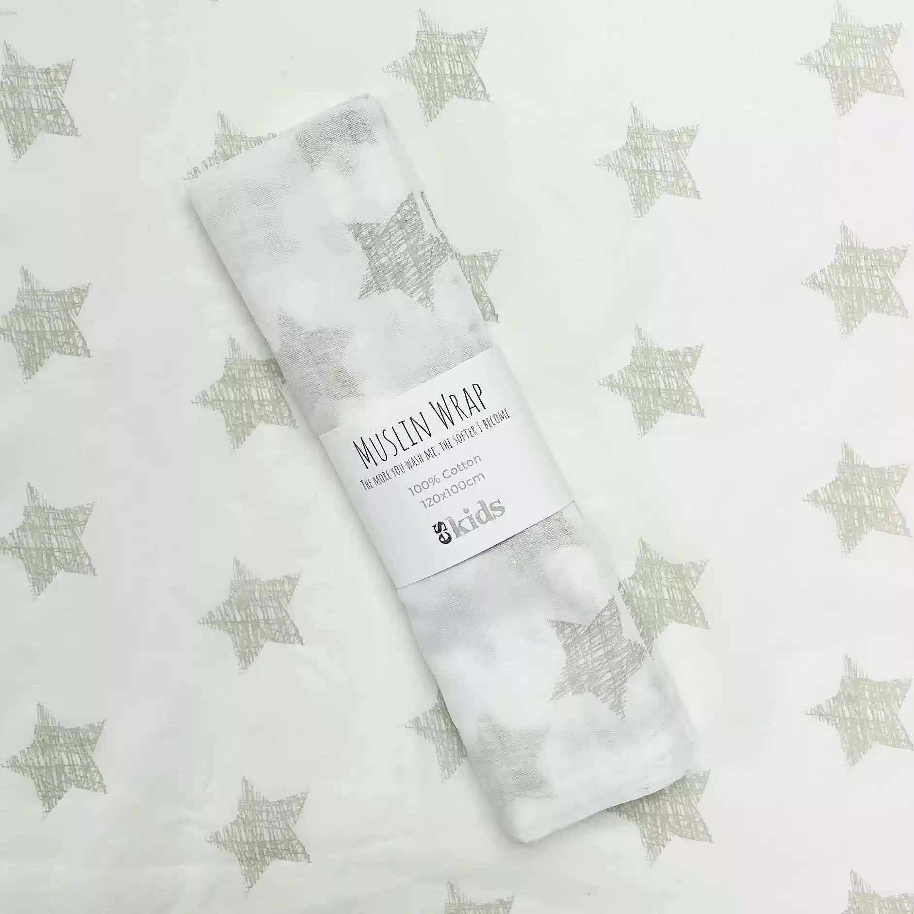 A delicately folded muslin wrap, featuring a charming star pattern, rests elegantly on coordinating fabric with the same celestial motif. The label displays "Muslin Wraps" from FlowersonNortonSt, emphasizing its 100% cotton composition—ideal for gently wrapping babies.