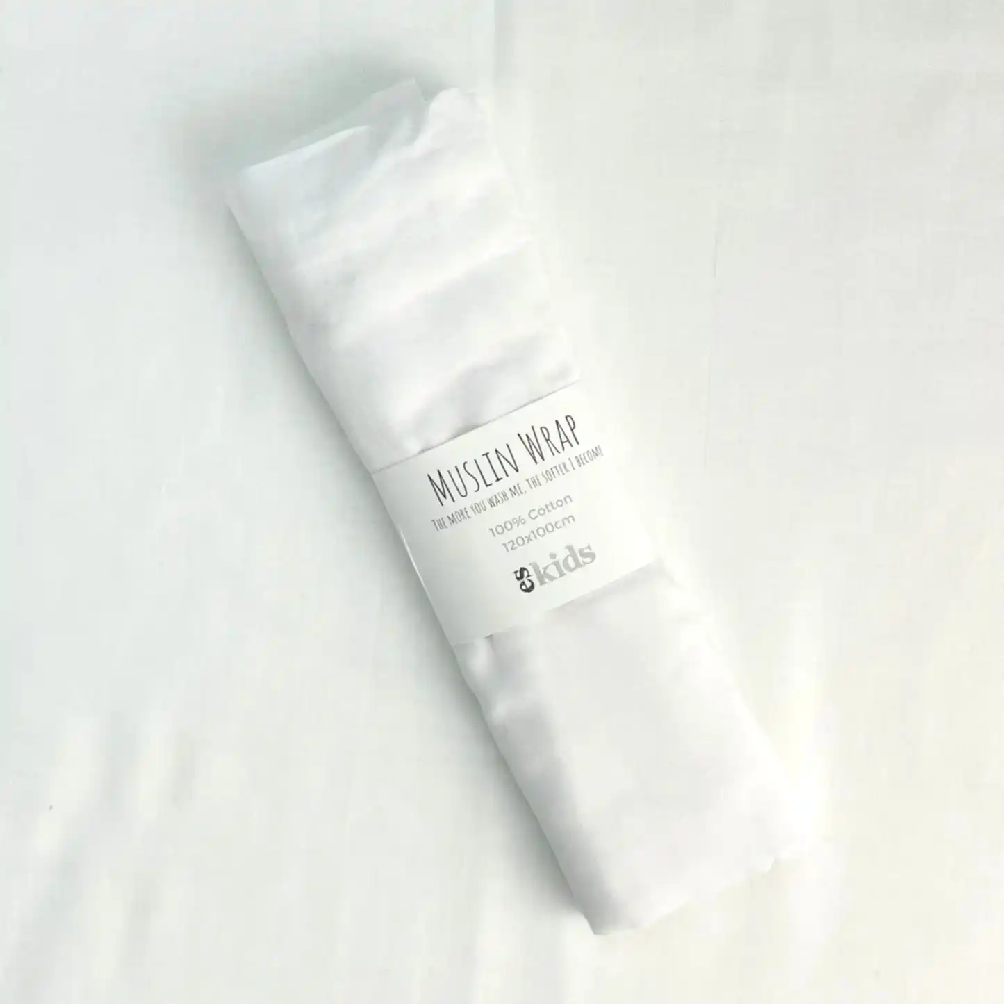 A soft Muslin Wrap from FlowersonNortonSt, rolled up with a label indicating it's 100% cotton, perfect for baby wrapping. The background is a plain white surface.