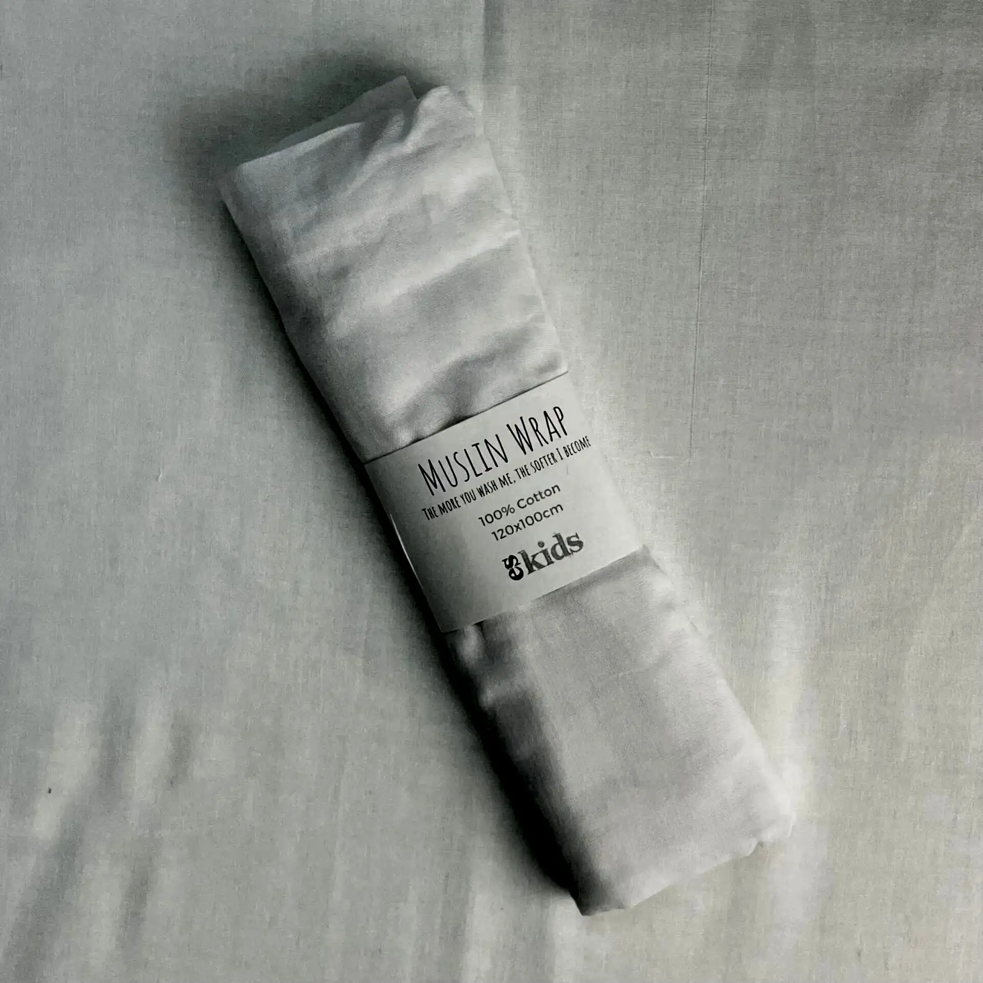 A soft Muslin Wrap from FlowersonNortonSt, rolled up with a label indicating it's 100% cotton, perfect for baby wrapping. The background is a plain white surface.