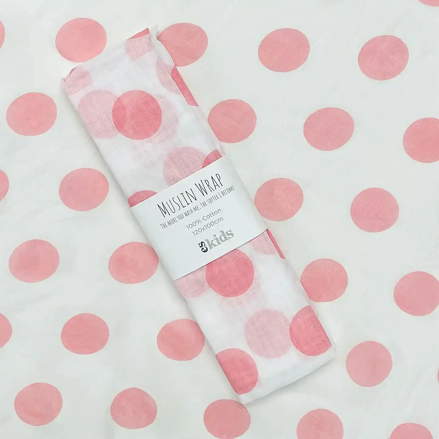 A Muslin Wrap from FlowersonNortonSt, adorned with a charming pink polka dot pattern, is rolled up and held together by a label. The background also features this delightful design, making it perfect for baby wrapping.