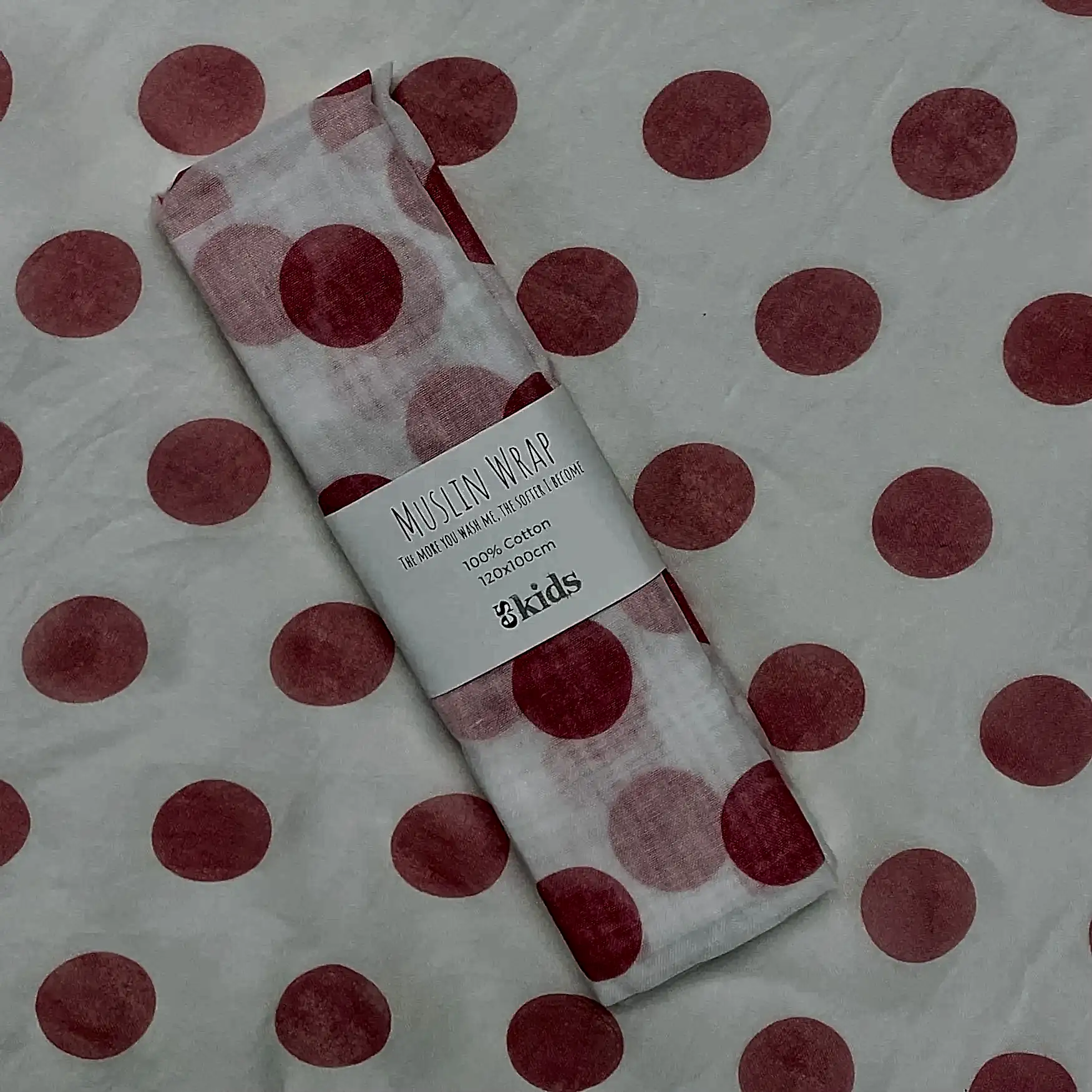 A Muslin Wrap from FlowersonNortonSt, adorned with a charming pink polka dot pattern, is rolled up and held together by a label. The background also features this delightful design, making it perfect for baby wrapping.